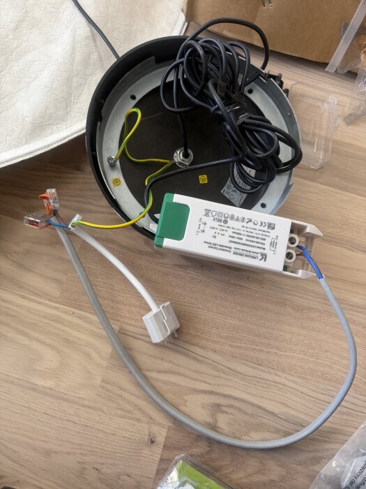 Elektrisk koppling med ledningar och transformator på ett trägolv, redo för installation.