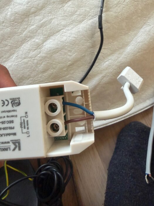 Elektrisk kopplingsdosa med synliga blå och bruna kablar anslutna, mot en träram med text och CE-märkning.