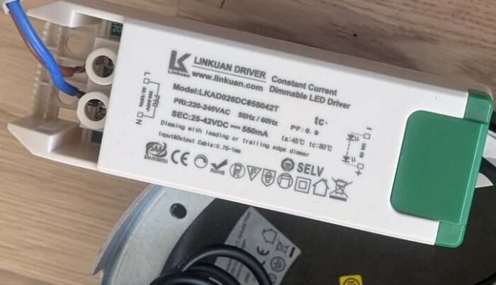 LED-drivare från Linkuan med specifikationer och säkerhetsmärkningar, modell LKA0D26DC055042T, med anslutna kablar, på ett trägolv.