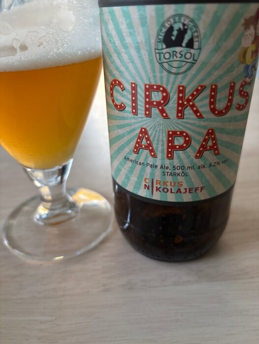 Flaska med etikett "Cirkus APA" från Torsöl mikrobryggeri och ett glas med ljus öl.