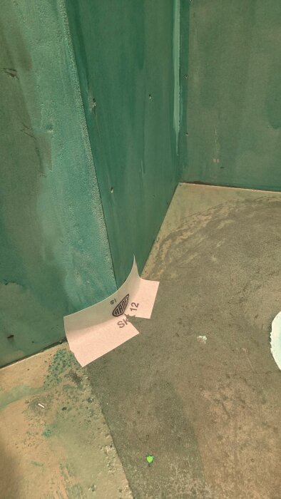 Green-painted rumsvägg och golv med ett märke av typen "ARDS SK12" på en golvremsa i ett renoveringsprojekt.