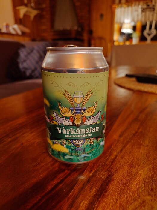 Burk med Vårkänslan american pale ale placerad på ett träbord i en träinredning. Etiketten visar natur- och djurmotiv.