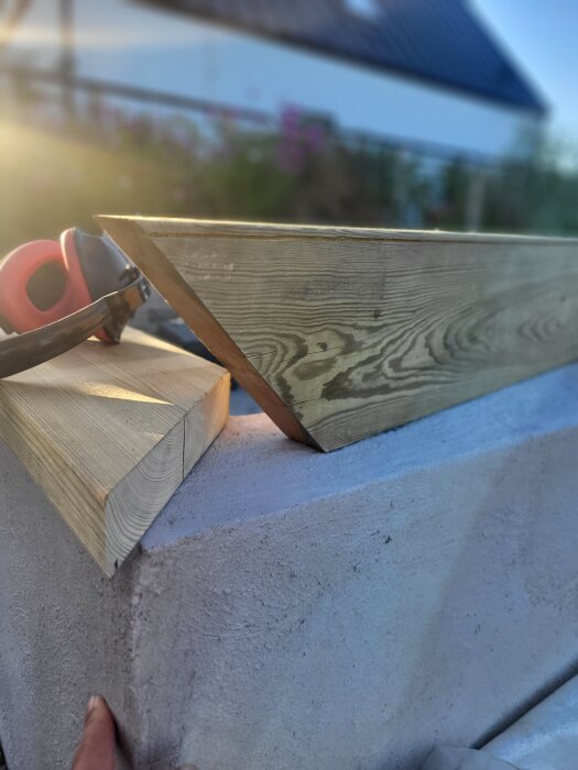 Träbitar med avfasade kanter på en betongblock, hörselskydd syns i bakgrunden under solnedgång.