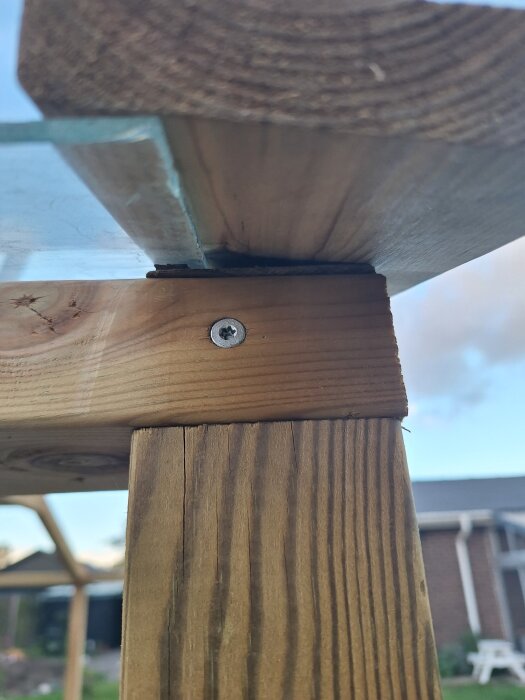 Träregel med monterat glas och skruv, del av hemmabyggt takfönster, synlig tätning och omgivande byggarbetsplats i bakgrunden.