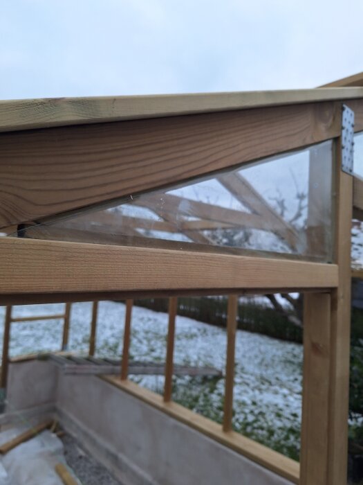 Träram och glasfönster under montering på veranda, med snötäckt gräsmatta i bakgrunden.