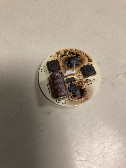 Bränd kretskort med elektroniska komponenter på en ljus yta, relaterat till reparation av en lampa och felsökning av belysningsproblem.