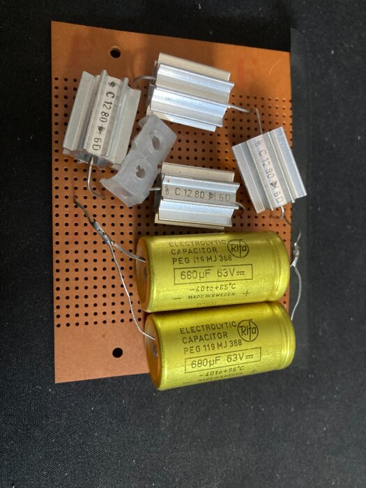 Elektroniska komponenter, inklusive motstånd och Rifa-kondensatorer, monterade på ett perforerat kretskort för en hemgjord transformatorreparation.
