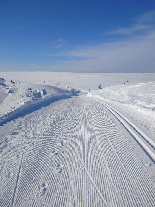Preparerat längdskidspår på en solig vinterdag med klarblå himmel och snötäckta vidder i bakgrunden.
