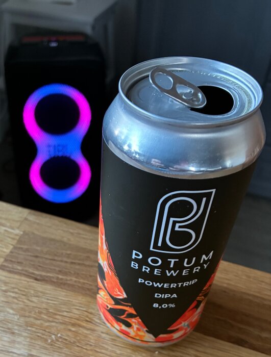 Öppen ölburk från Potum Brewery med etiketten "Powertrip DIPA 8,0%". I bakgrunden syns en högtalare med neonfärgade ljus.
