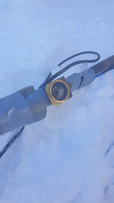 Ett fryst rör utomhus insvept i tejp och isolering, liggande på snö.