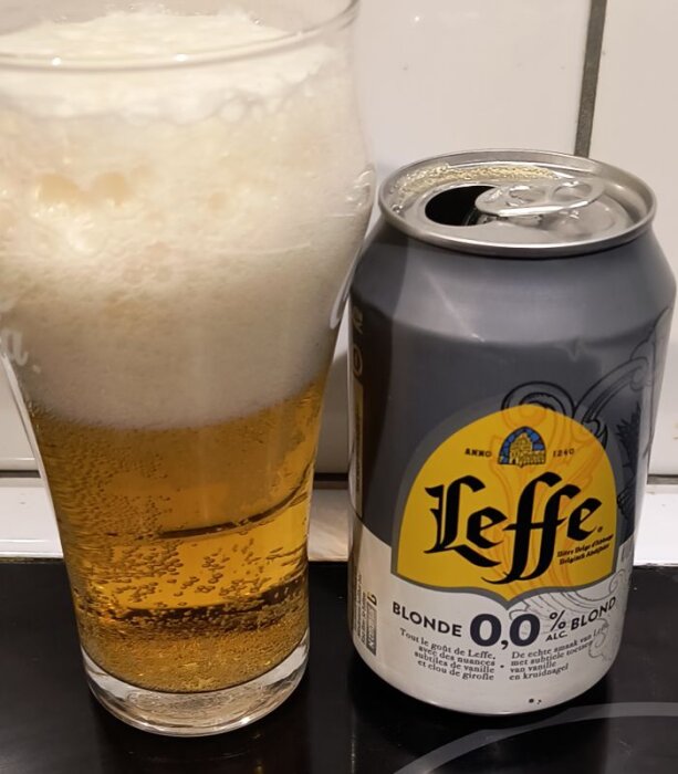Ölglas med skummande alkoholfri Leffe Blonde bredvid en öppnad burk på en köksbänk.
