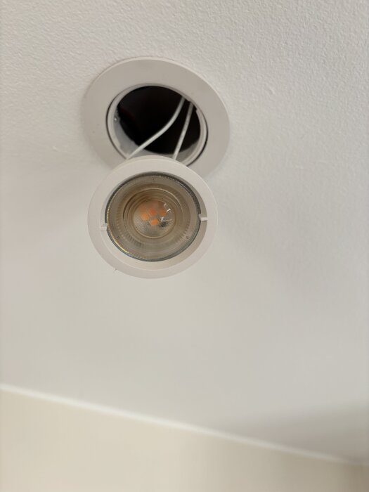 Brunfärgad LED-spotlight i taket med synlig brännskada och smält plast, delvis urkopplad från sin installation.