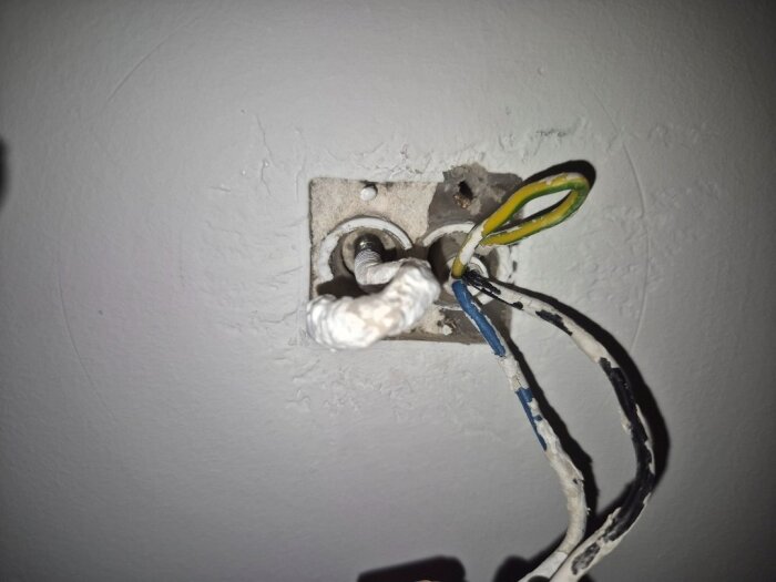 Vägguttag med synliga ledningar och jordad kabel, två rörutgångar i en betongvägg, en röringång har en gänga för krok.
