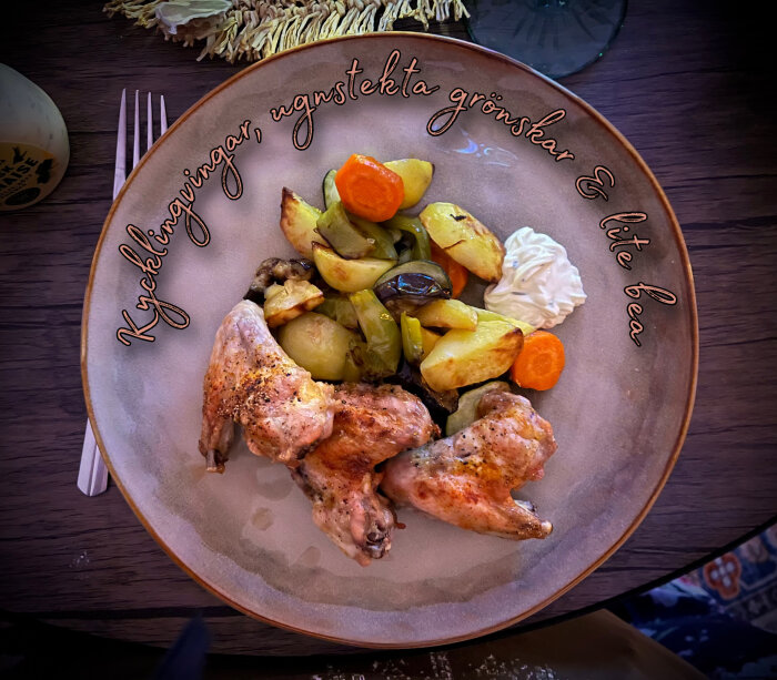 Kycklingvingar med ugnsstekta grönsaker, inklusive potatis och morötter, serveras på en tallrik med en klick bearnaisesås.
