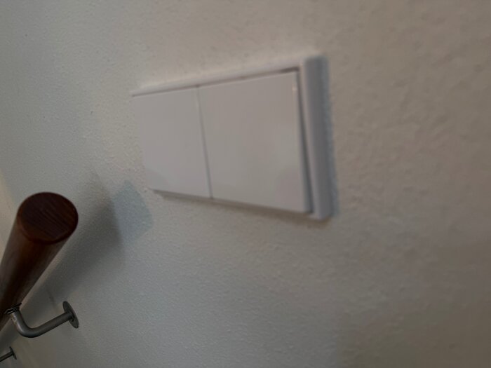 Vita Jung strömbrytare av plast monterade på en vägg, fotograferade i närbild bredvid en träräcke.