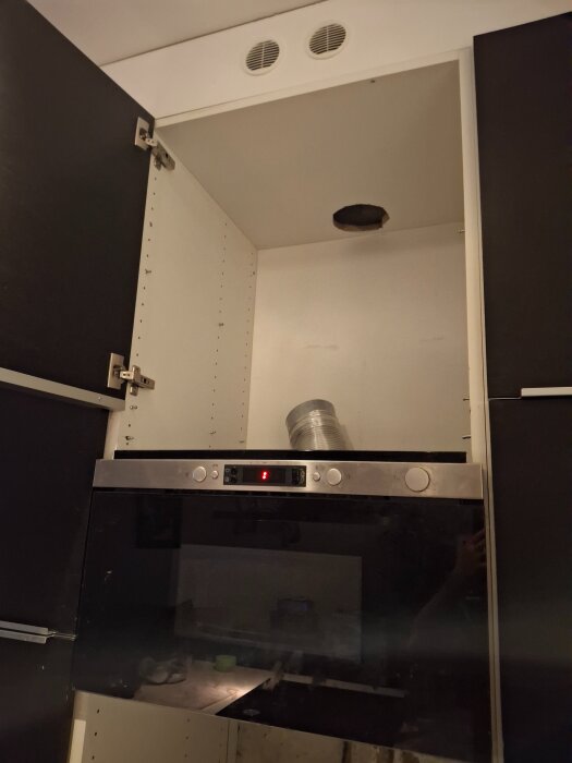 Öppet skåp ovan mikrovågsugn med rör kopplat från ventilationshål till överdelen av ett köksskåp.