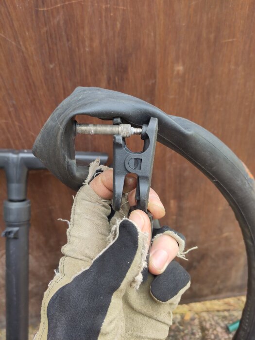 Verktyg användas för att ta bort en cykelslang med ventil, hålls av en hand i arbetshandske.