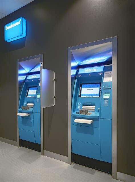 Två blå bankomater monterade i en vägg, med skylten "Bankomat" ovanför, användbara för uttag av kontanter.