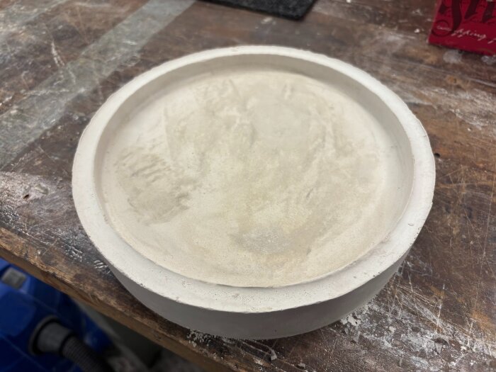 Rund gipsform på en arbetsbänk, redo för glasfusing eller slumpning, med en slät insida och synliga ådringar.