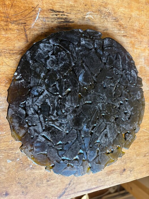 Delvis smält glasplatta på träyta, resultat av glasfusing-experiment mellan olika temperaturer, där individuella bitar fortfarande är synliga.