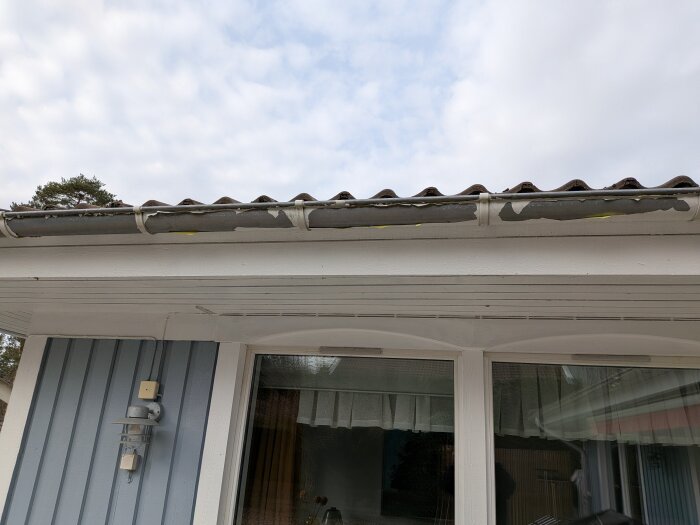 Färgen flagnar på hängrännan på ett valmat tak från ett LB-hus från 1991; främst framkanten och mellan rännkrokarna är påverkade.