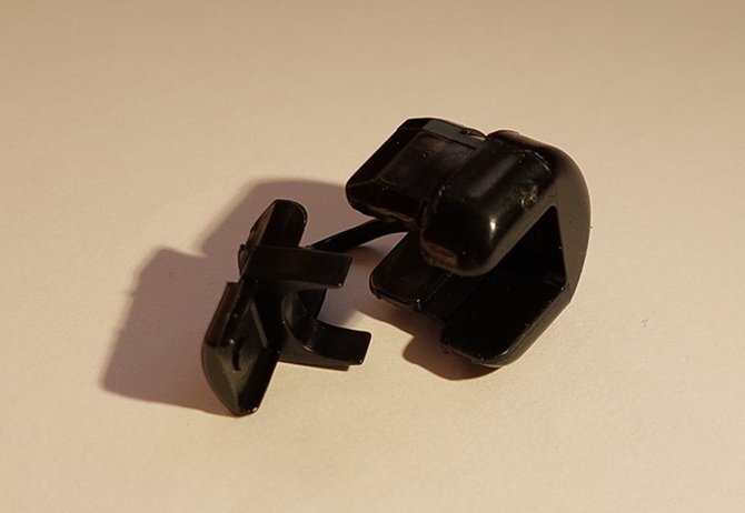 Två svarta plastklips liggande på en yta, avsedda för att fästa kablar i en bordssåg enligt instruktionen om installation av mjukstart.