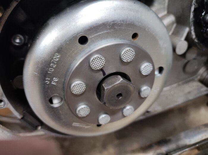 Närbild av en mopeds svänghjul med mutter, en tvättpolett används som lock för att reparera en varvräknare.