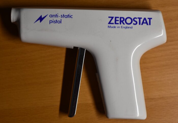 En vit antistatpistol av märket Zerostat, tillverkad i England, ligger på ett träbord.
