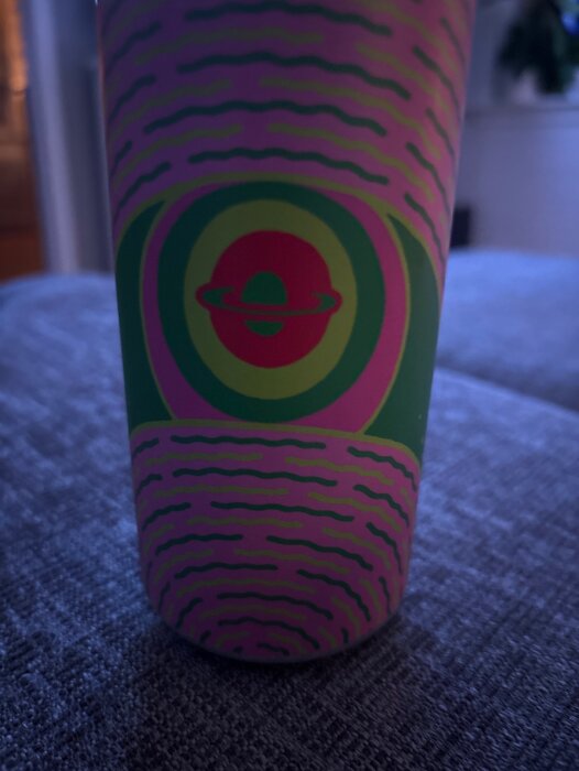 En färgglad Omnipollo cup med vågigt mönster och en ringplanet i mitten.
