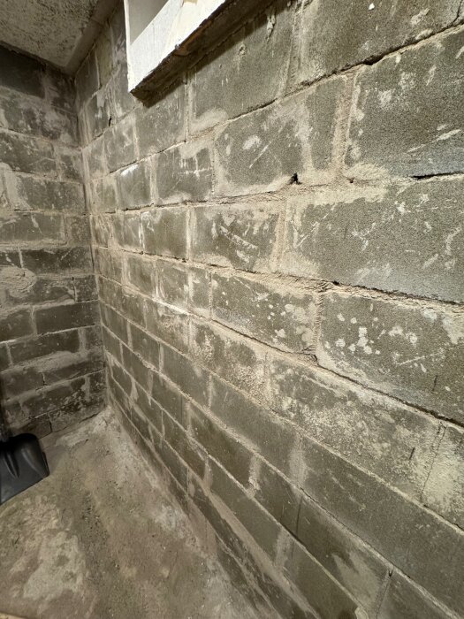 Vägg av betonghålsten eller lecablock i en källare med ojämn yta och hål, del av pågående renovering för ventilerat golv och puts på väggarna.