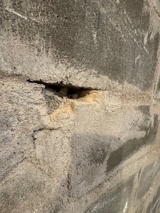 Vägg med oregelbunden yta och ett större hål, möjligtvis i betonghålsten eller lecablock, inom ett renoveringsprojekt i källaren.