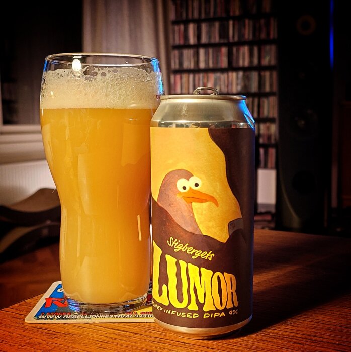 Ölglas bredvid en burk med etikettmotiv av en fågel och texten "Stigbergets LUMOR honey infused DIPA 9%".