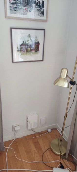 Hörn av rum med golvlampa, tavlor på väggen, internetutrustning och kablar vid väggen, visar en installation på undervåningen.
