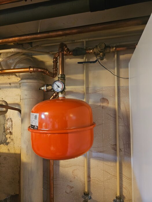 Röd expansionskärl med kopparrör och tryckmätare, del av värmesystem i hus.