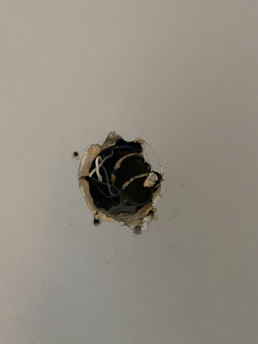 Rund hålighet i vägg med exponerade elledningar, troligen för installation av eluttag eller belysningsarmatur.