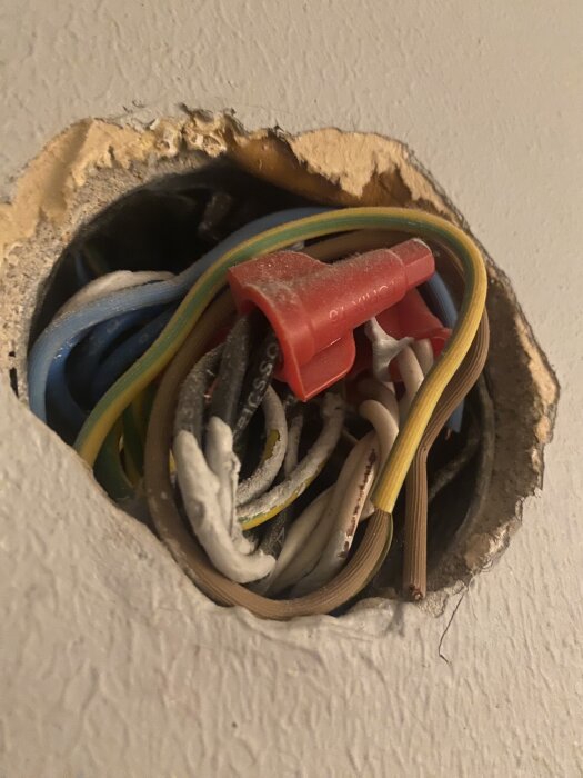Elektriska kablar i olika färger med röd kopplingshylsa synliga genom ett hål i en vägg.