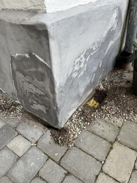 Fuktig husgrund med flagande färg och synlig grusfyllning runt grunden.