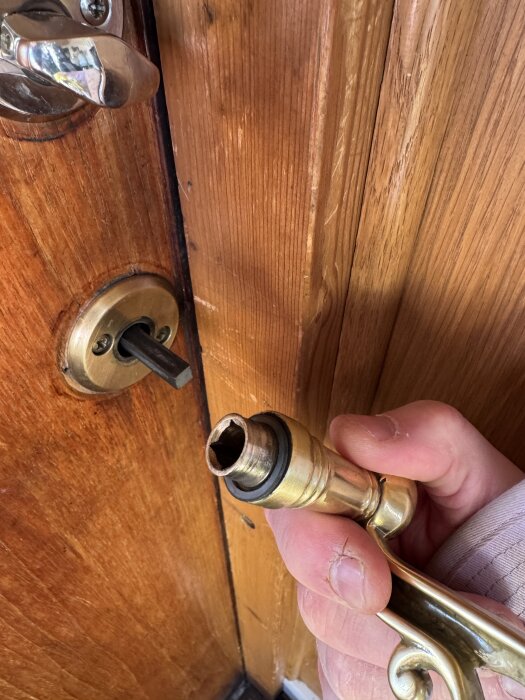 Närbild av en dörr med ett löst handtag som hålls i handen, utan synliga skruvar, på insidan av en träfärgad dörr.