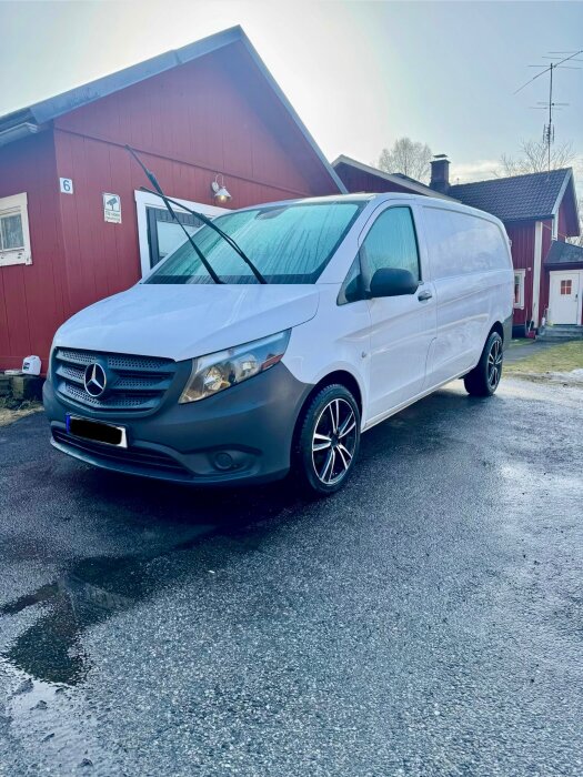 Vit skåpbil med Mercedes-logotyp parkerad framför ett rött hus, avspolad men utan att ha gnuggats, i soligt väder.