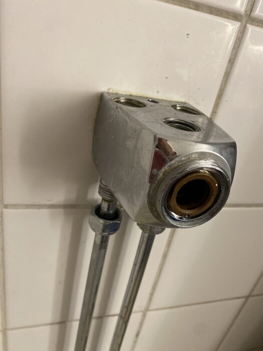 Väggmonterad gammal duschblandare med exponerade rör och skruvhål mot vit kakel.