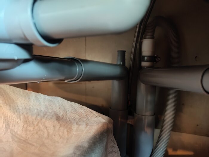 VVS-installation under diskbänk med synliga rör och en läcka.