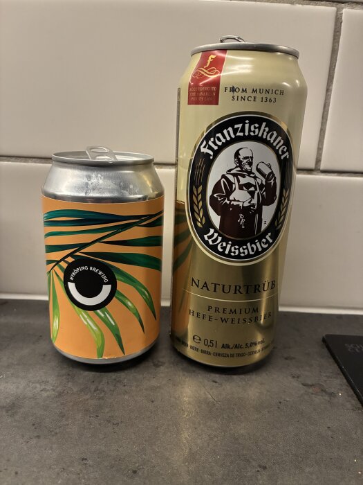 Två ölburkar, en med tropiskt motiv från Linköping Brewing och en Franziskaner Weissbier, mot en kaklad vägg.