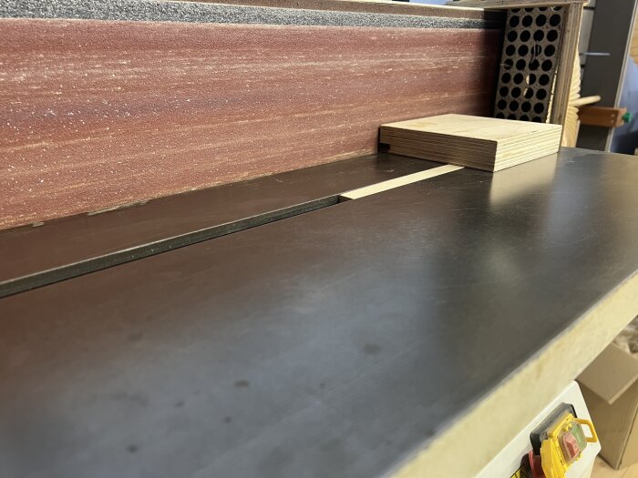 Kinesisk bandputs-slipmaskin inställd i 90 grader med slätt gjutjärnsbord och träbit, mot bakgrund av röd sandpapperyta.