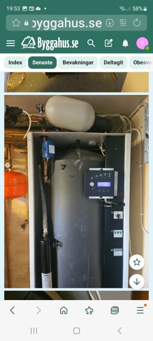 Blå växelventil uppe till vänster i ett värmesystem, med tank och kontrollpanel i en inomhusinstallation.