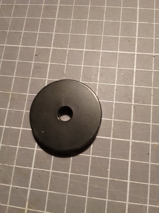 Svart adapter för vinylsinglar ligger på ett rutigt underlag.