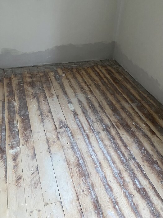 Gammalt trägolv i furu eller gran, med fernissa, färg- och spackelfläckar, del av renoveringsprojekt i lägenhet.