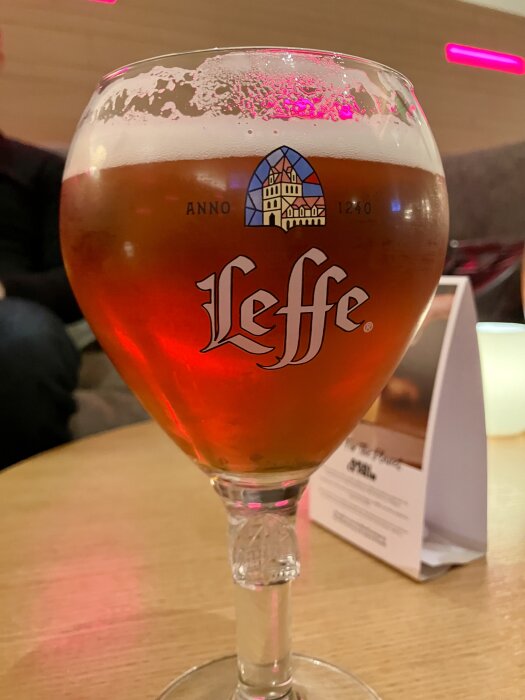 Ett stort glas rött öl med Leffe-logotypen på ett bord.
