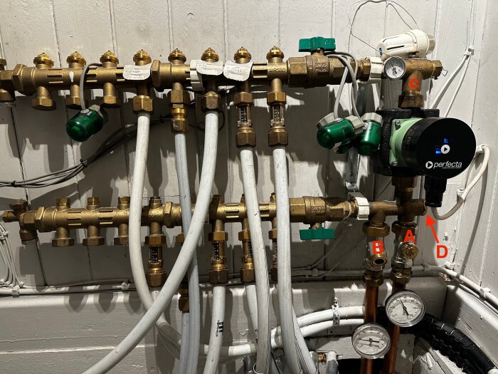 Golvvärmesystem med rör, tryckmätare och pumpar. Etiketter visar positioner A, B, C och D. Perfekta pump i fokus, flera ventiler synliga.