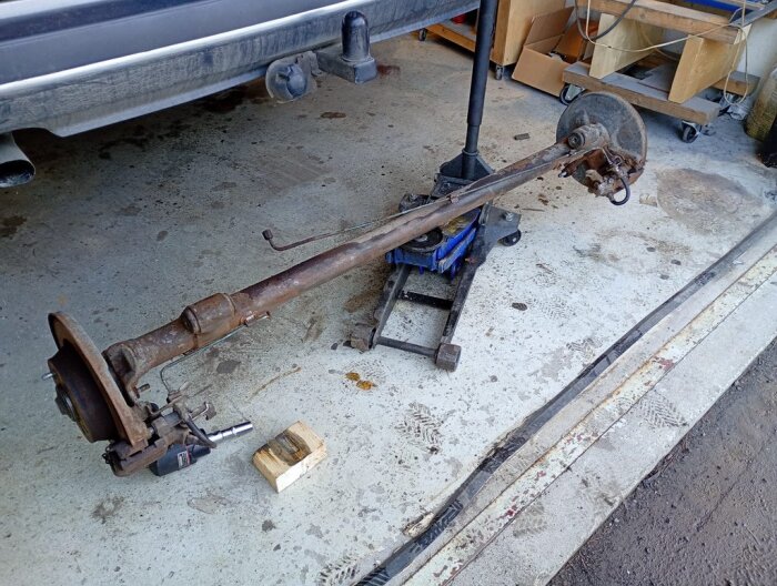 Bakaxel från en Saab lyfts ur med domkraft för att undersöka upphängningen; garagets golv synligt i bakgrunden.