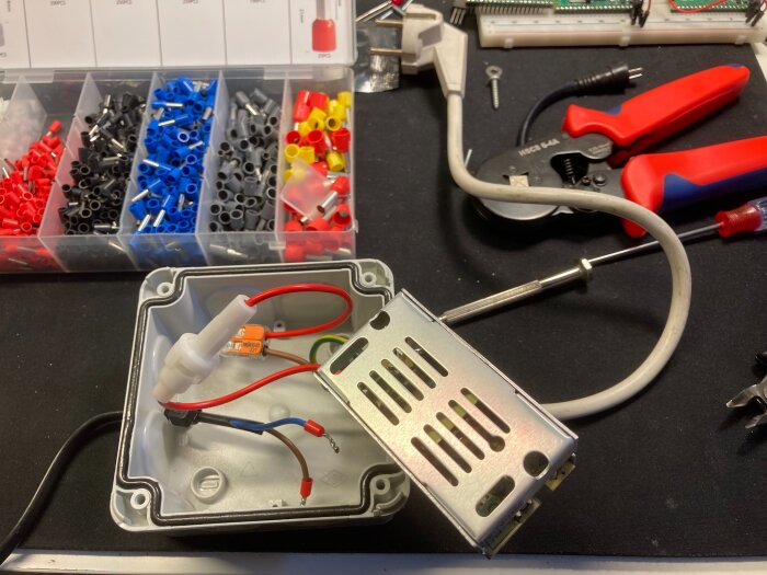 En kopplingsdosa med elektronik och kablar, omgiven av verktyg som kabelsaxar och hylsor i en organiserad sorteringslåda.